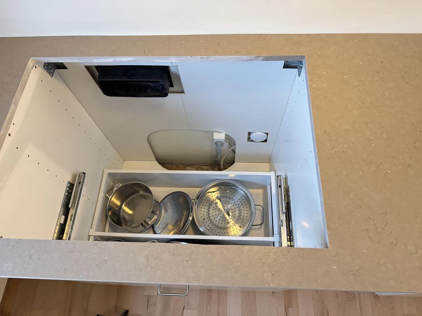 Närbild av rektangulärt urtag i polerad Silestone Coral Clay ovanför öppna köksstommar och låda med kastruller i Ganløse.