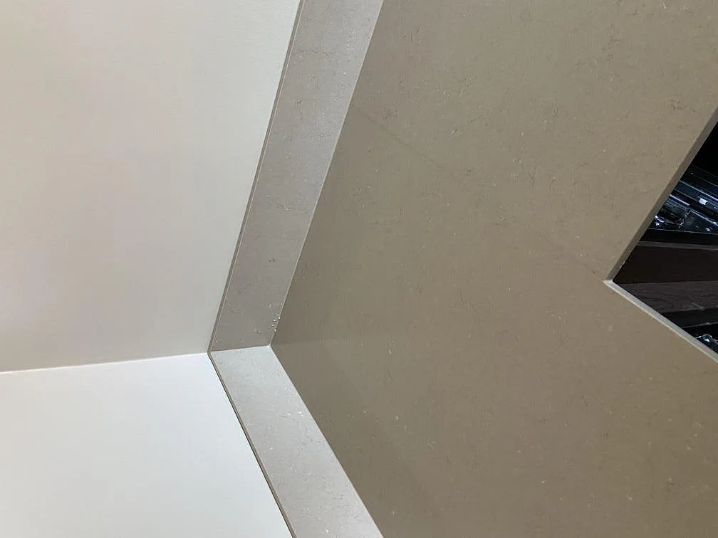 Hörn av köksbänkskiva i polerad Silestone Coral Clay med uppvikt stänkkant mot vit vägg i Göteborg.