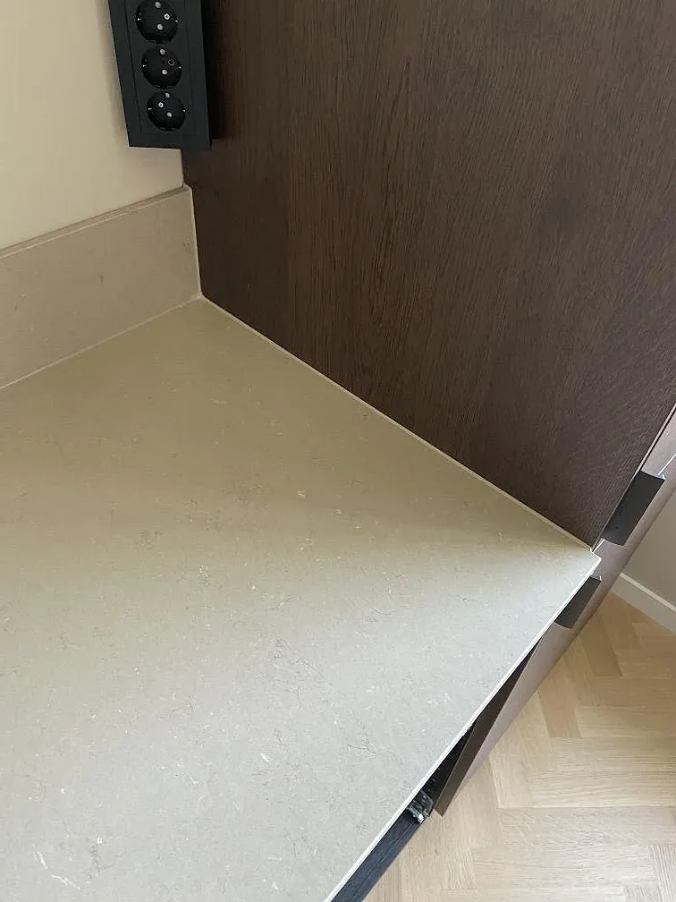 Kant på greige Silestone Coral Clay köksbänkskiva mot mörkbruna träfronter och fiskbensgolv i Göteborg.