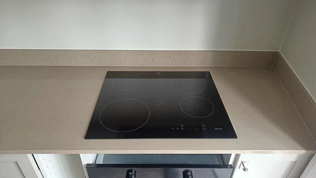 Infälld induktionshäll i polerad Silestone Coral Clay med uppvikt stänkkant i ett hörn av ett kök i Göteborg.