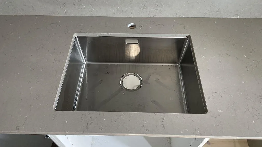 Underlimmad rostfri diskho i polerad Silestone Coral Clay komposit med matchande stänkskydd i ett kök i Göteborg.
