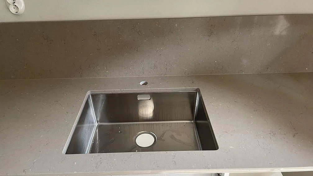 Sidodel av polerad Silestone Coral Clay köksbänkskiva med låg gråbeige stänkkant och vita köksstommar i Göteborg.