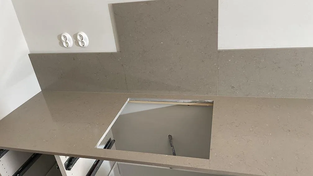 Närbild av gråbeige Silestone Coral Clay kompositbänkskiva med stänkskydd, öppen diskhoutsågning och rostfri diskho vid kanten i Göteborg.