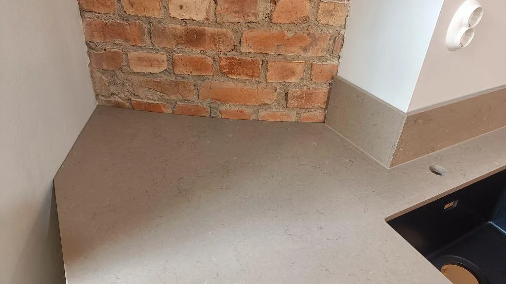 Polerad Silestone Coral Clay vid synlig tegelvägg, svart diskho och uppvikt stänkkant i ett Göteborgskök under montering.