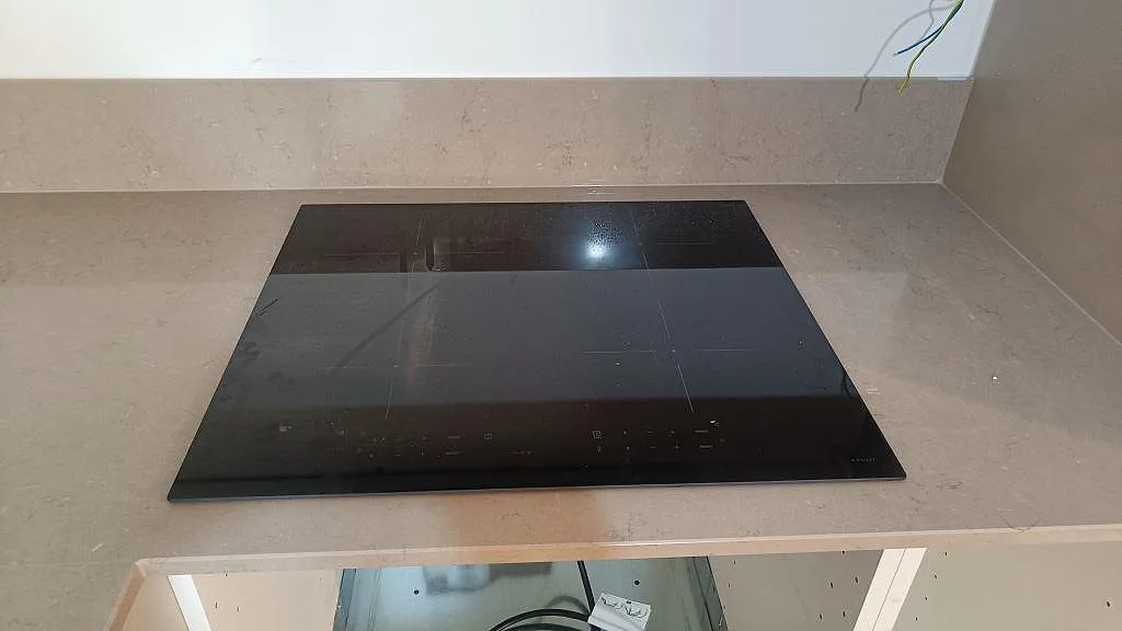 Svart induktionshäll vid polerad Silestone Coral Clay och uppvikt stänkkant i ett kök i Göteborg.