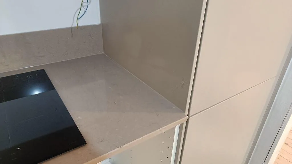 Avslut vid högskåp med polerad Silestone Coral Clay, svart induktionshäll och uppvikt stänkkant i ett Göteborgskök.