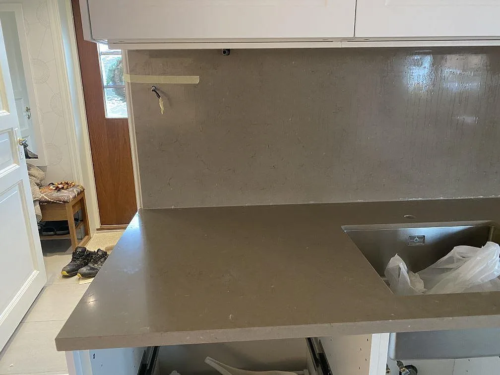 Översikt av köket i Grebbestad under montering med en lång bänkskiva i Silestone Coral Clay längs väggen.