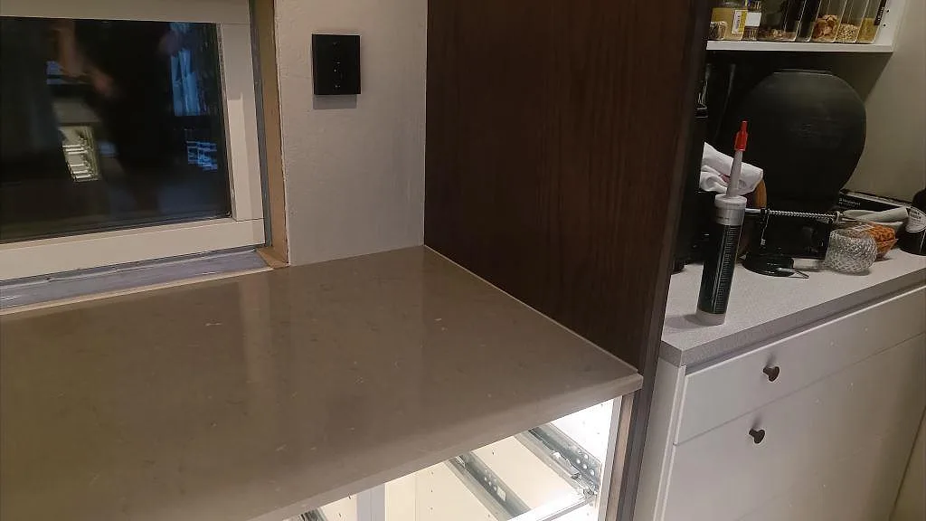 Bakre bänkrad i polerad Silestone Coral Clay med fönster, mörkt trä och ljusa lådfronter i Habo.