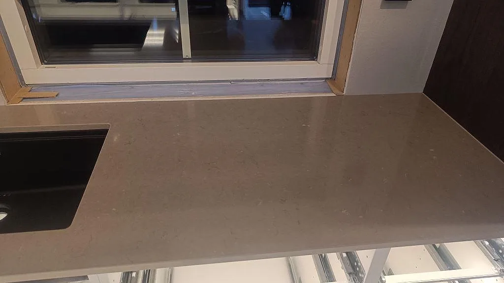 Bänkskiva i polerad Silestone Coral Clay vid fönster, med ljusa stommar och varm gråbeige komposityta i Habo.