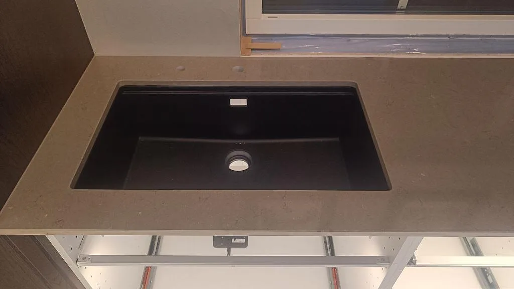 Underlimmad svart diskho i polerad Silestone Coral Clay, gråbeige kompositbänkskiva vid fönster i Habo.