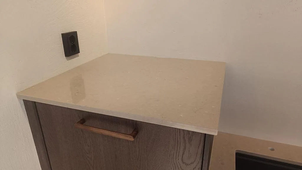 Sidobänk i polerad Silestone Coral Clay på mörkt träskåp bredvid diskzonen i ett kök i Habo.