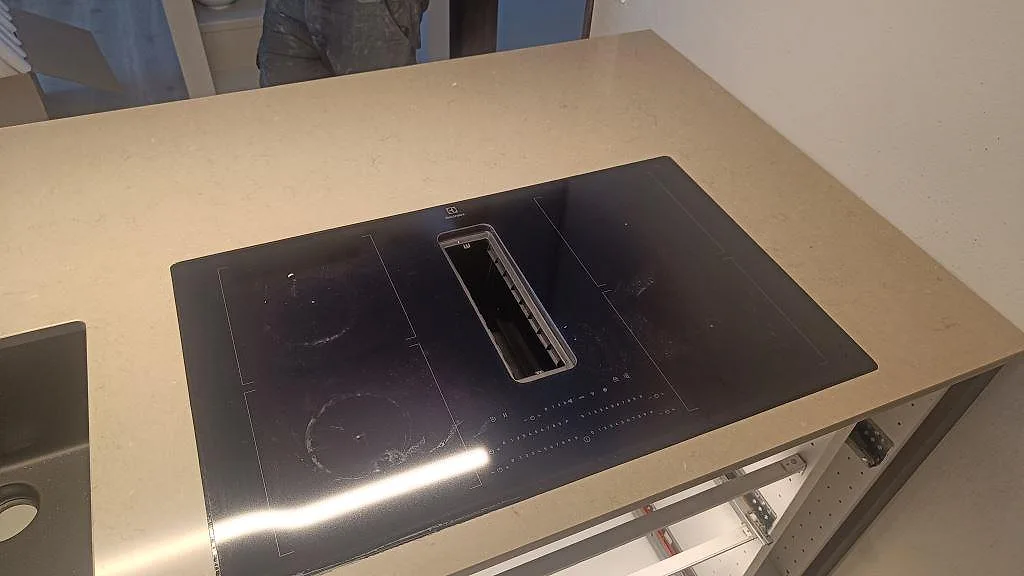 Köksö i polerad Silestone Coral Clay med svart häll och synlig gråbeige komposit runt installationen i Habo.