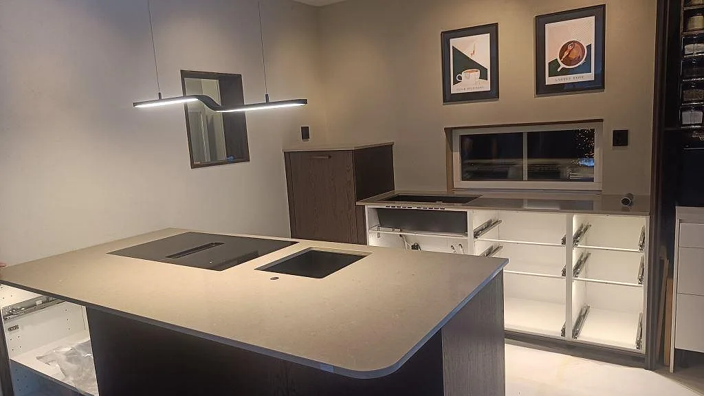 Köksö och bänkskiva i polerad Silestone Coral Clay, gråbeige komposit, med svart diskho och induktionshäll i ett kök i Habo.