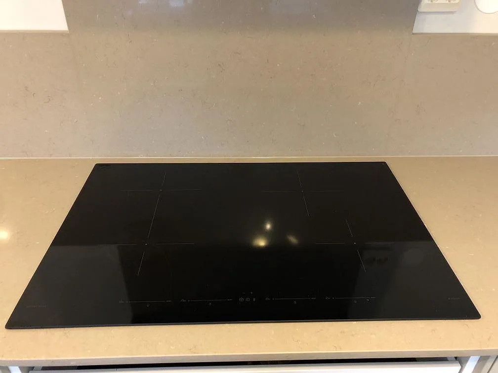 Induktionshäll monterad ovanpå en polerad bänkskiva i Silestone Coral Clay i ett kök i Hällingsjö.