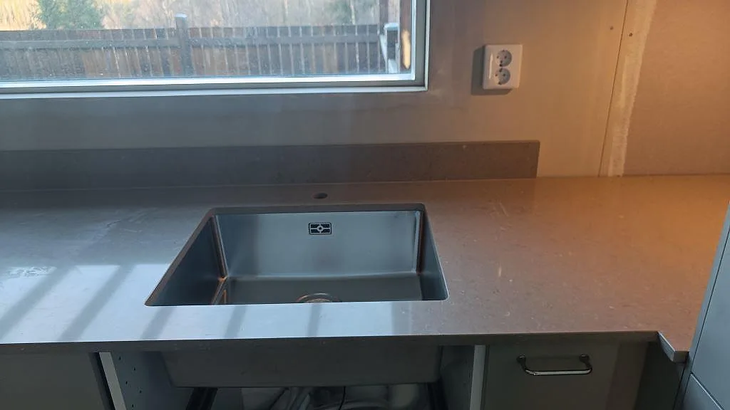 Polerad Silestone Coral Clay i ett kök i Härryda med rostfri diskho under fönster och matchande stänkskydd i samma komposit.