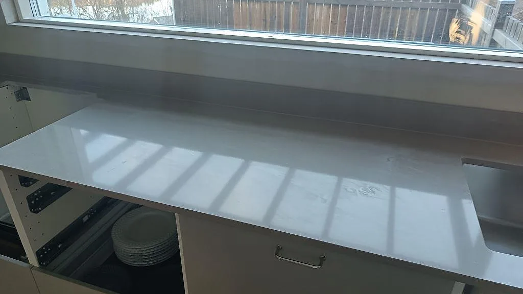Lång arbetsyta i polerad Silestone Coral Clay, varm gråbeige komposit, med fönsterljus och synlig diskhokant i ett kök i Härryda.