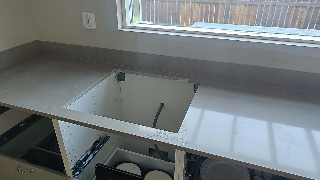 Köksbänkskiva i polerad Silestone Coral Clay, kvartskomposit, med öppen hällhåltagning och stänkskydd under fönster i Härryda.