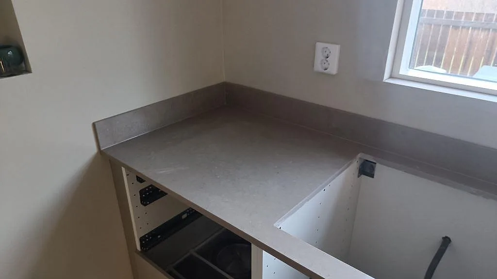 Hörnvy av köksbänkskiva i polerad Silestone Coral Clay, gråbeige komposit, med håltagning och uppvikt stänkkant i Härryda.