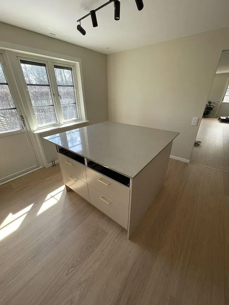 Köksö med polerad bänkskiva i Silestone Coral Clay och lådfronter framför ett fönster i ett ljust kök i Hässelby.