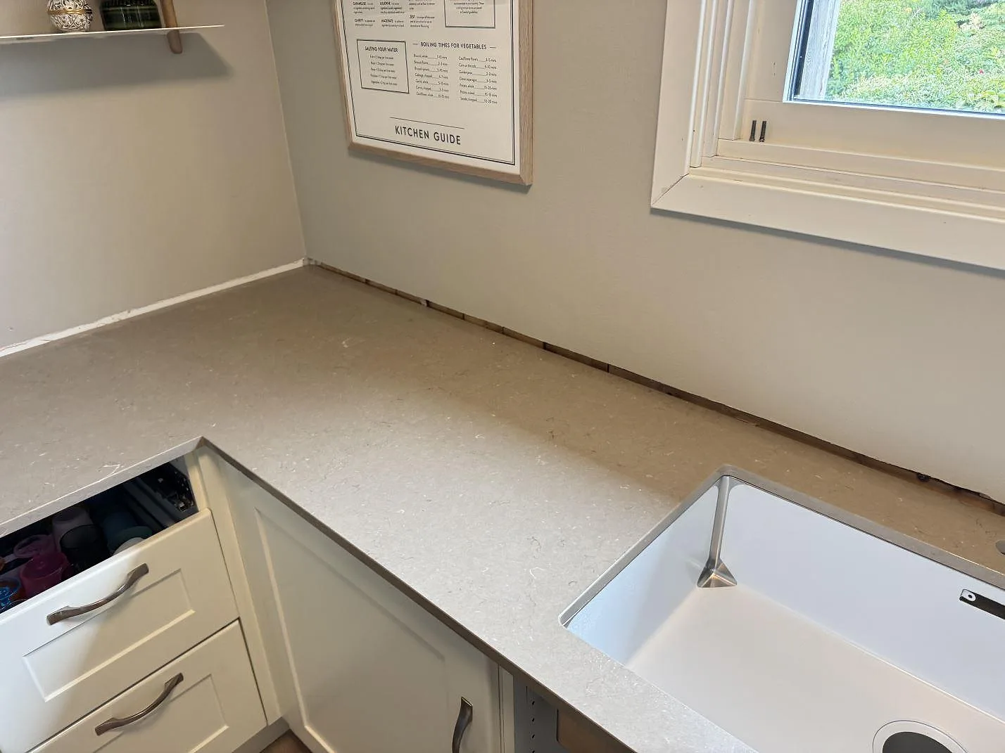 Hörndel av köksbänkskiva i Silestone Coral Clay, polerad kvartskomposit, vid fönster och vit inredning i Hisings Backa.
