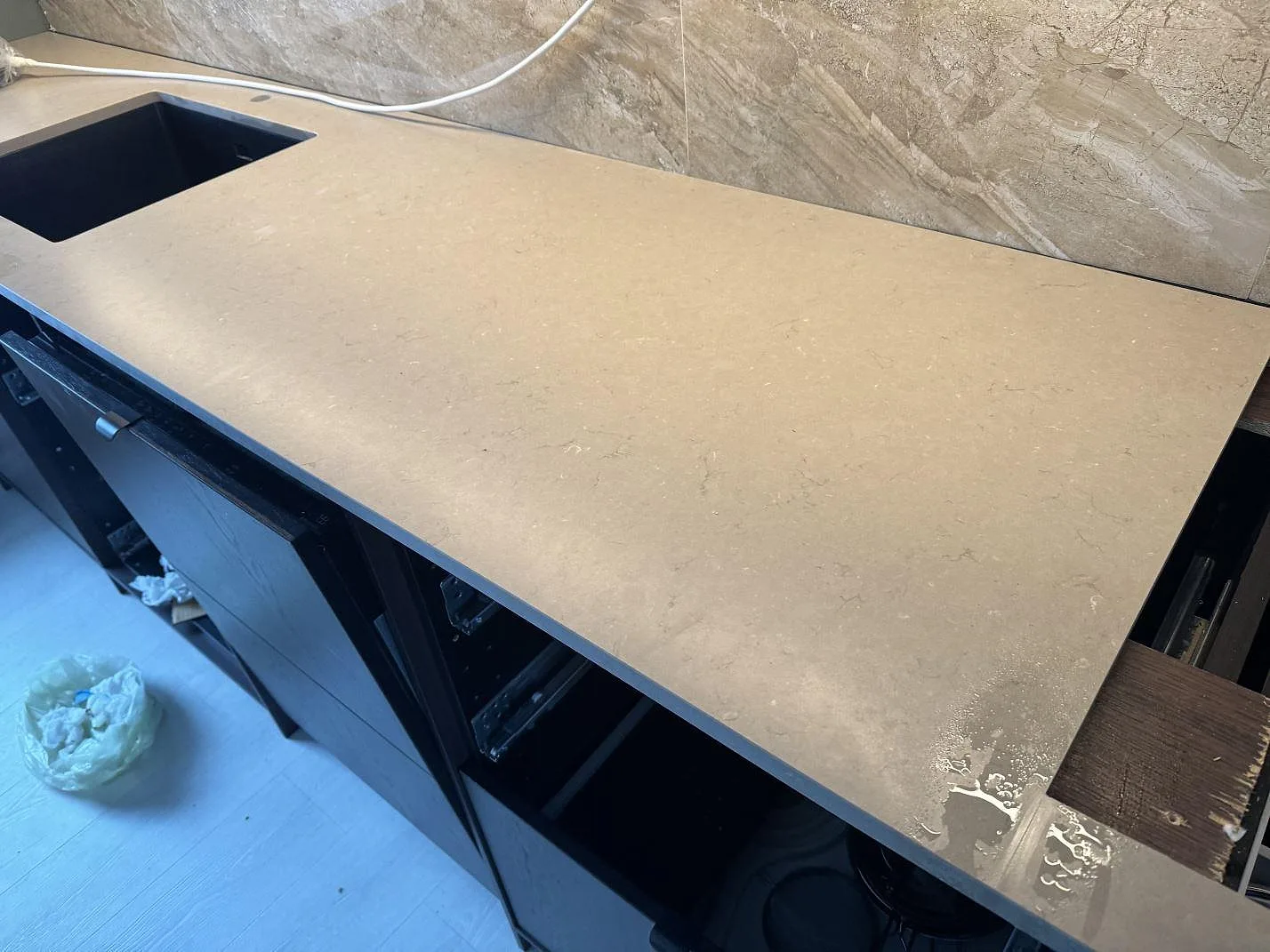Lång väggbänk i Silestone Coral Clay, matt greige komposit, med diskhozon vid vänster kant och marmorerat kakel under montering i Höganäs.