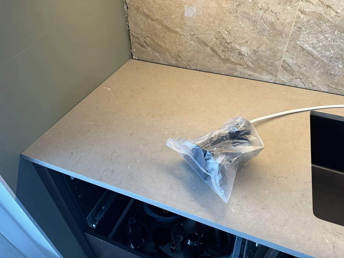 Detalj av Silestone Coral Clay bänkskiva vid svart underlimmad diskho och grön sidovägg under montering i Höganäs.