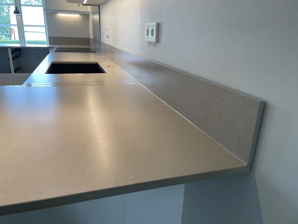 Lång köksbänk i Silestone Coral Clay med uppvikt stänkskydd, svart diskho och svart häll i Höllviken.