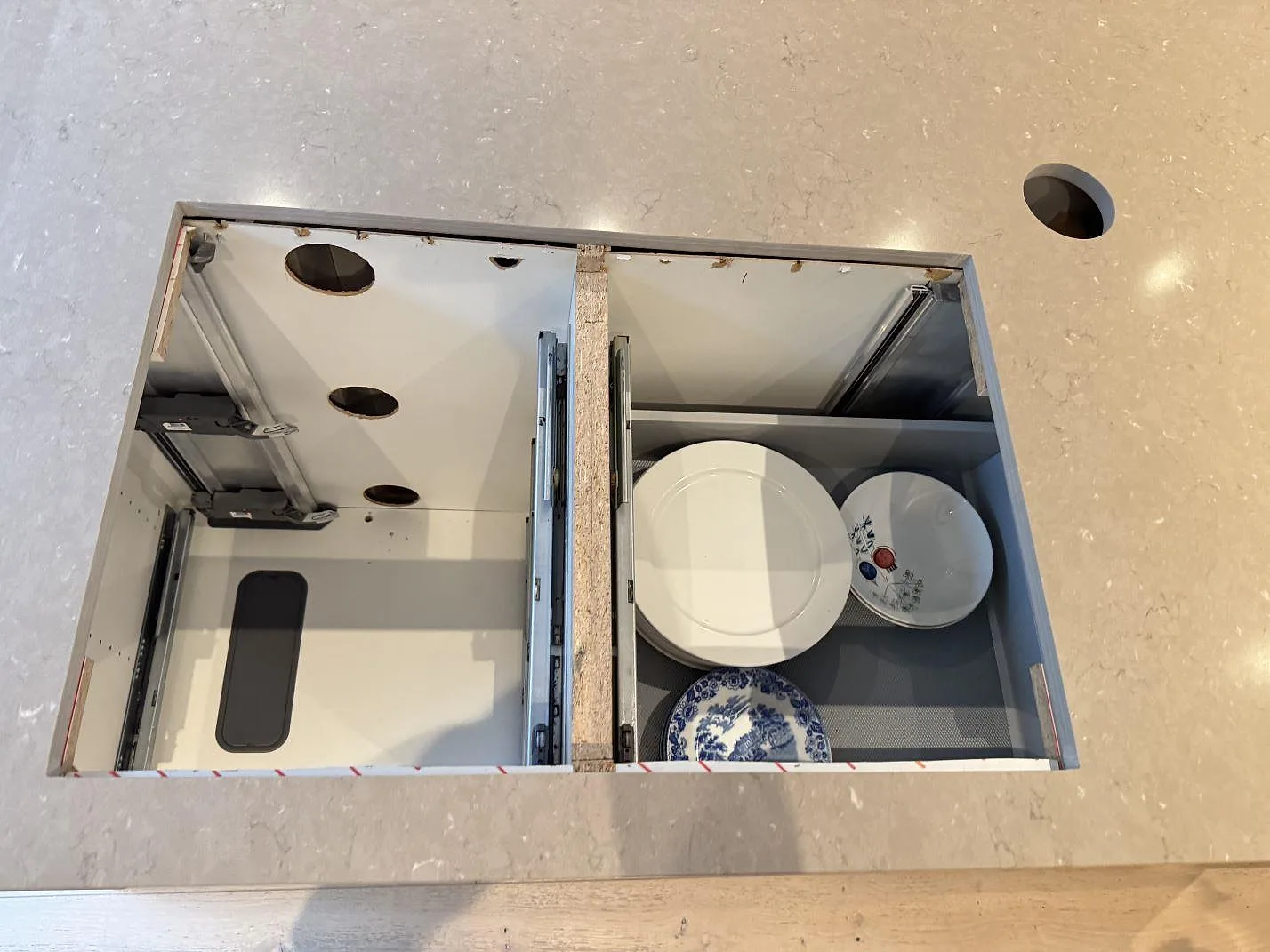 Ovanifrån syns köksbänkskiva i Silestone Coral Clay, polerad komposit, med rektangulära urtag och öppna skåpstommar i Höllviken.