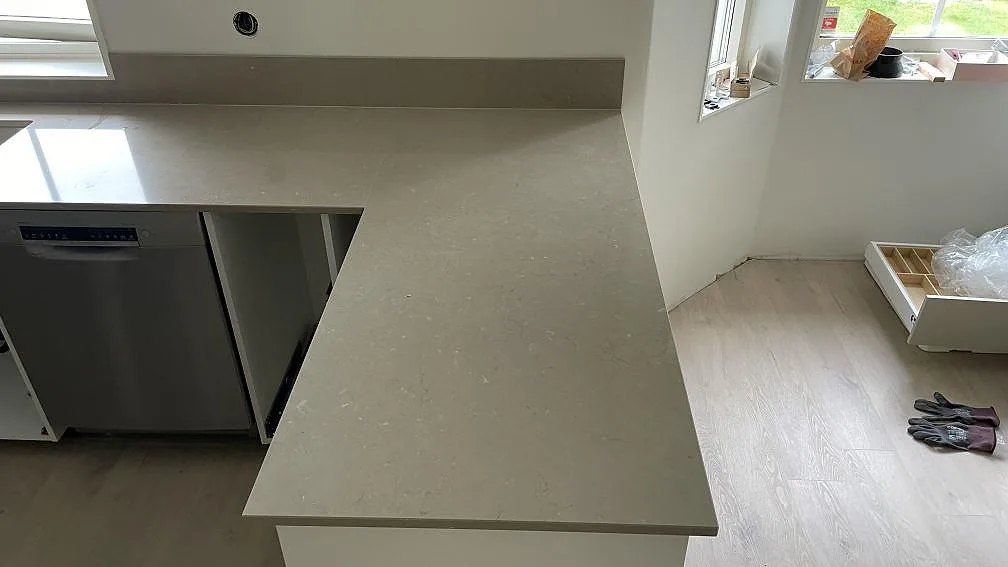 Lång arbetsyta i polerad Silestone Coral Clay med gråbeige ådring och låg stänkkant i köket i Höör.