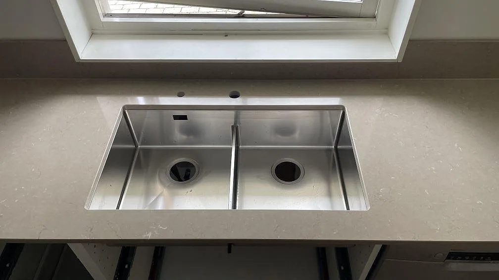 Polerad Silestone Coral Clay som köksbänkskiva med rostfri dubbelho under fönstret i ett kök i Höör.