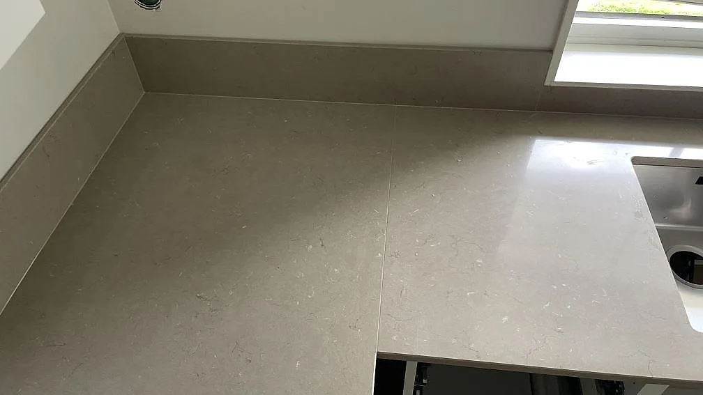 Hörndel i polerad Silestone Coral Clay med låg stänkkant och rostfri diskho delvis synlig i köket i Höör.
