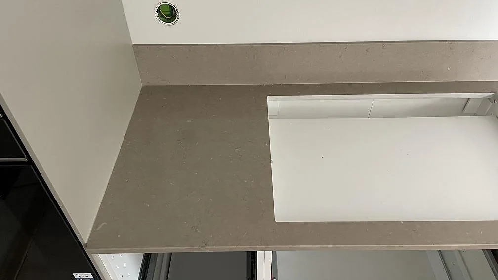 Detalj av hällöppning och gråbeige polerad Silestone Coral Clay med stänkkant i kök i Höör.