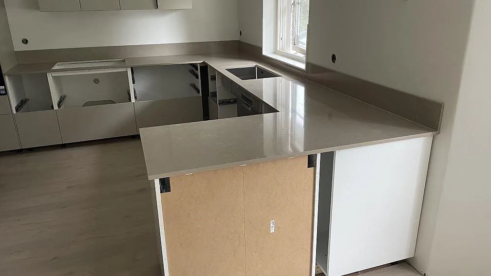 Köksbänkskiva i polerad Silestone Coral Clay med låg stänkkant, rostfri diskho och hällöppning i ett kök under montering i Höör.