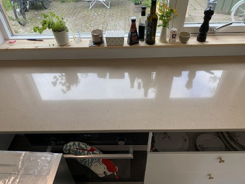 Polerad köksbänkskiva i Silestone Coral Clay vid fönstret med tydlig spegling och ugn under, i ett kök i Hørsholm.