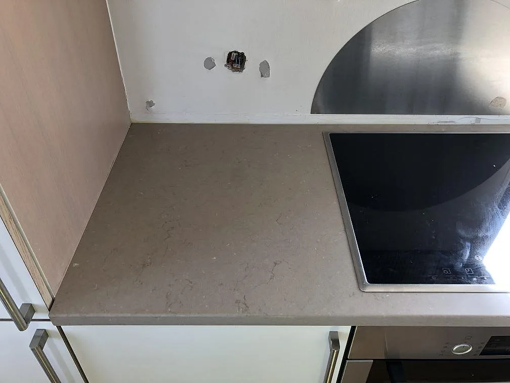 Bänkskiva i taupe Silestone Coral Clay med infälld induktionshäll mot bar vägg under montering i ett kök i Holbæk.