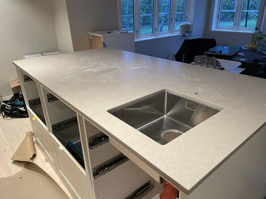 Stor köksö i Silestone Coral Clay, Mocka, med rostfri diskho och ljusa skåpstommar under montering i Vetlanda.
