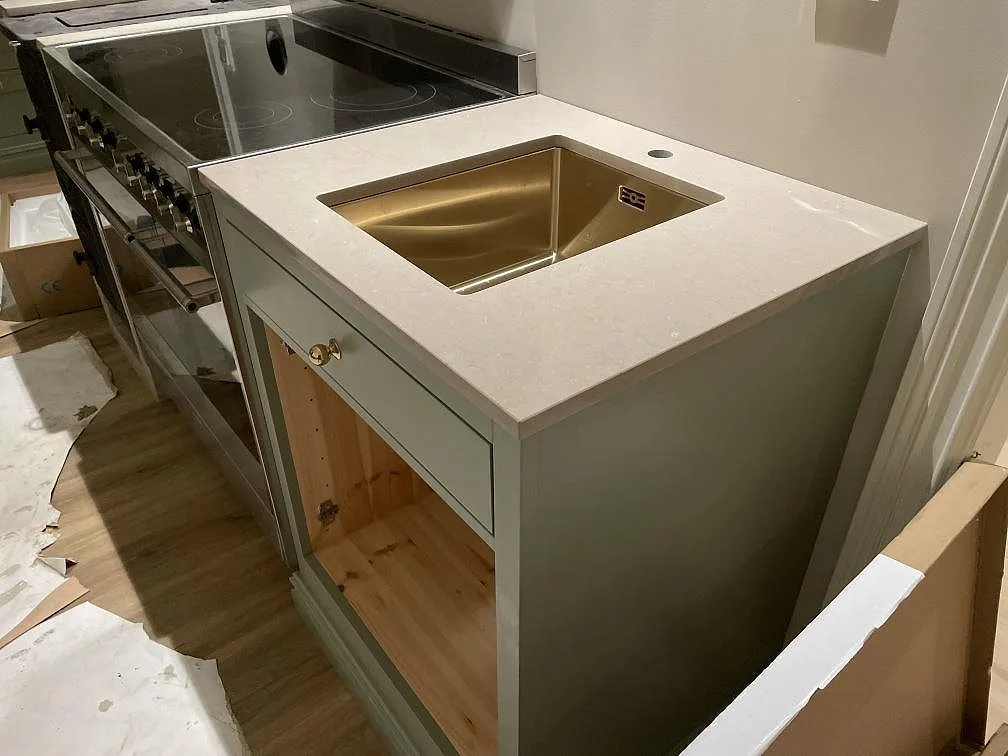 L-formad köksbänkskiva i polerad Silestone Coral Clay komposit med mässingsfärgad underlimmad diskho och spis intill i Holsbybrunn.