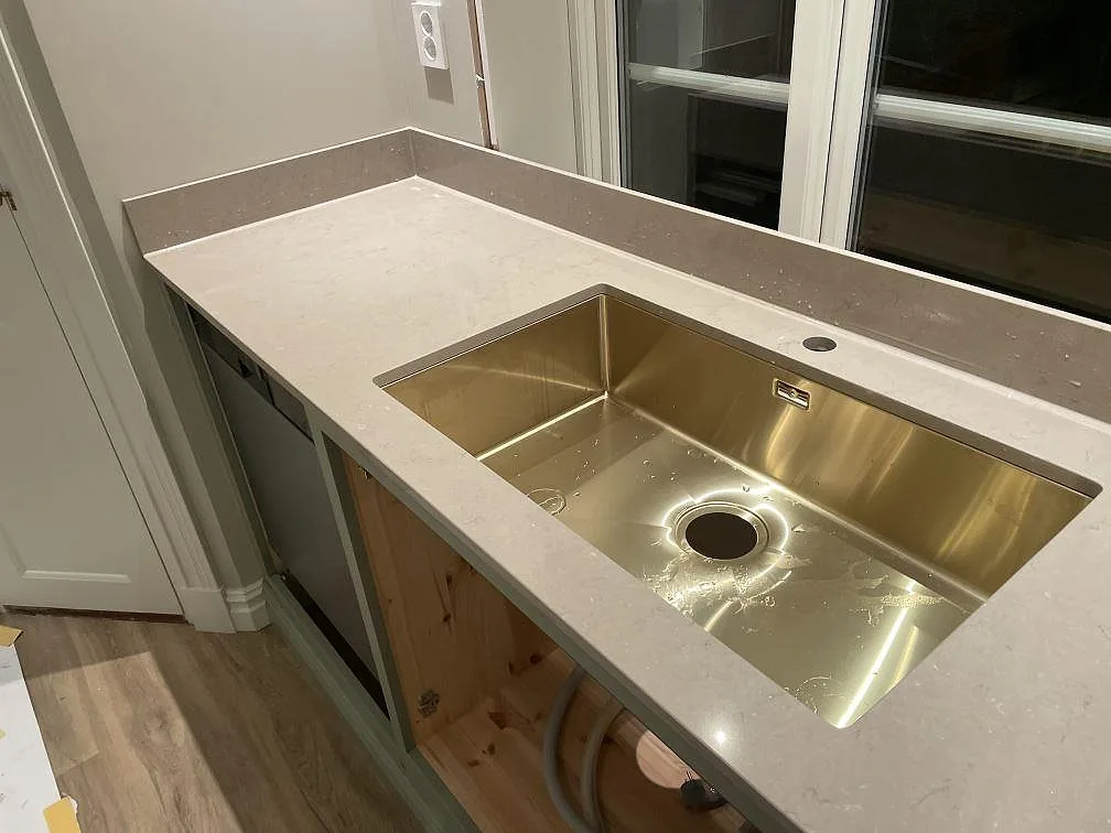 Polerad Silestone Coral Clay bänkskiva med underlimmad mässingsfärgad diskho och lågt stänkskydd vid fönster i Holsbybrunn.