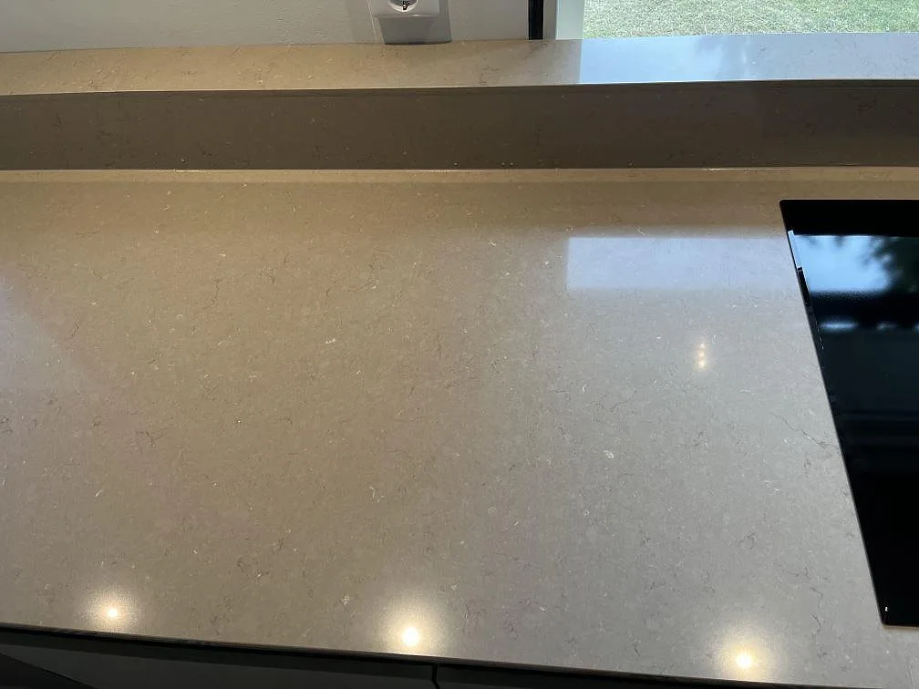 Polerad Silestone Coral Clay köksbänkskiva med diskret ådring och svart induktionshäll mot fönstret i ett kök i Ingelstad.