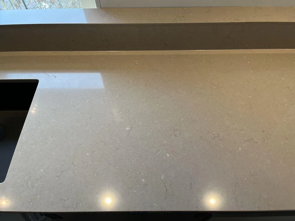 Greige Silestone Coral Clay köksbänkskiva med uppvikt stänkkant och svart häll, polerad yta, i ett kök i Ingelstad.
