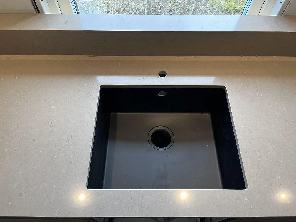 Underlimmad svart kompositdiskho i polerad Silestone Coral Clay köksbänkskiva med förborrat blandarhål i ett kök i Ingelstad.