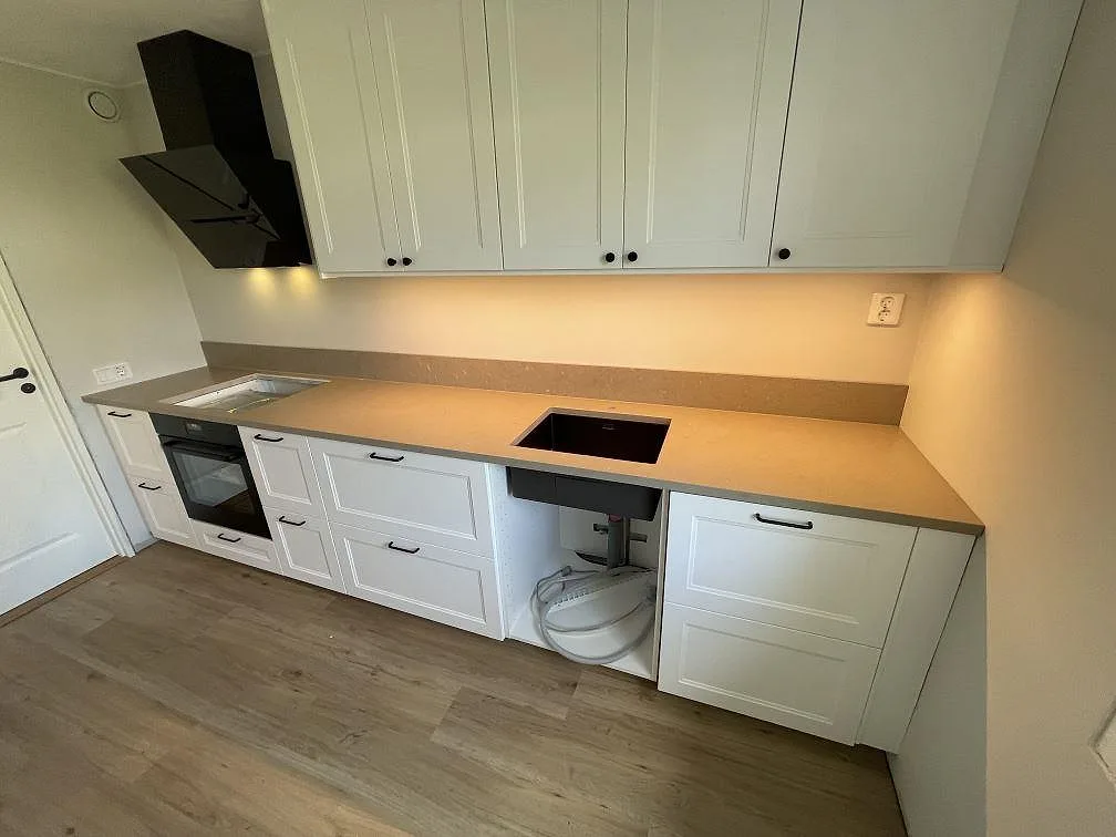 Köksbänkskiva i taupegrå Silestone Coral Clay komposit, matt Mocka, med underlimmad diskho, häll och uppvikt stänkkant i ett kök i Järfälla.