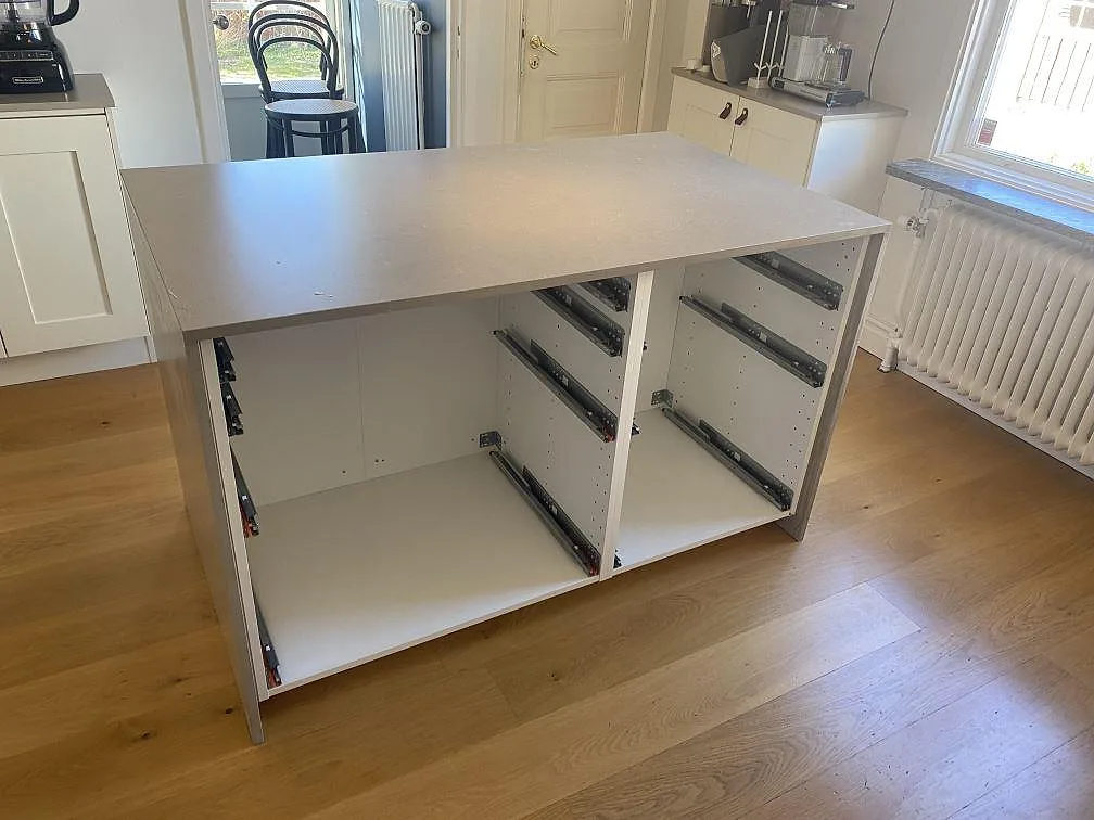 Köksö med bänkskiva i matt Silestone Coral Clay komposit och öppna stommar under montering i Jönköping.