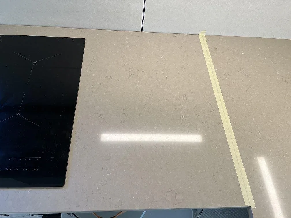 Infälld induktionshäll i en köksbänkskiva av matt Silestone Coral Clay med greige kakelfront bakom, kök i Kållered.