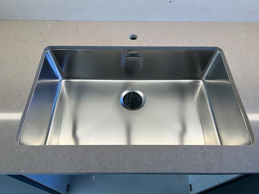 Underlimmad rostfri enkeldiskho i en köksbänkskiva av Silestone Coral Clay med separat blandarhål borrat i stenen, kök i Kållered.