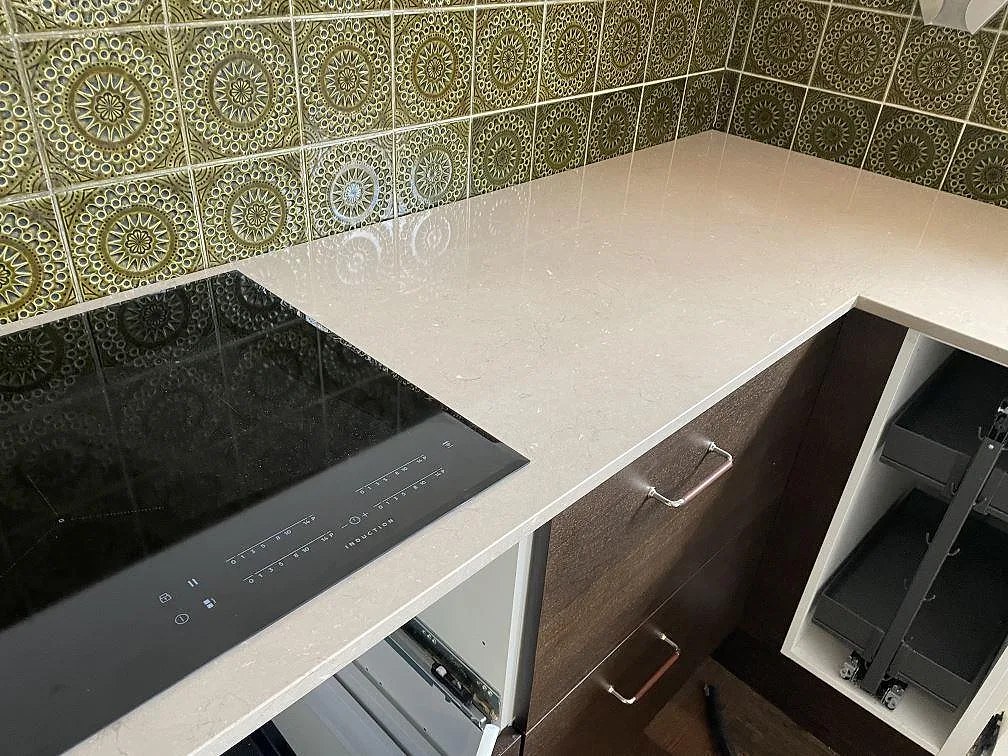 Svart induktionshäll i polerad köksbänkskiva av Silestone Coral Clay komposit mot grönt mönstrat kakel i Kållered.