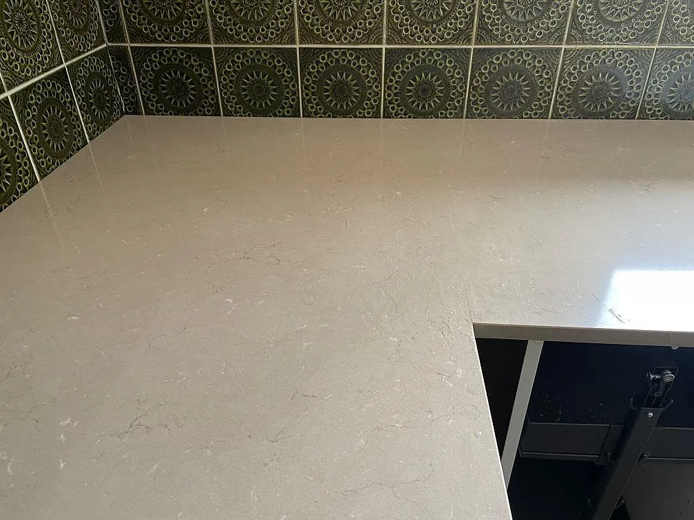 Närbild på polerad Silestone Coral Clay komposit vid väggbänk och grönt kakel, med ljus ådring i ytan, Kållered.