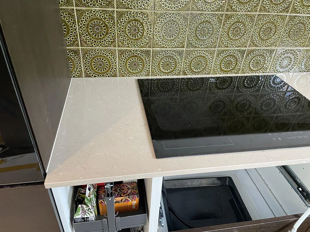 Detalj av svart induktionshäll infälld i polerad Silestone Coral Clay komposit vid kökets gröna kakel i Kållered.