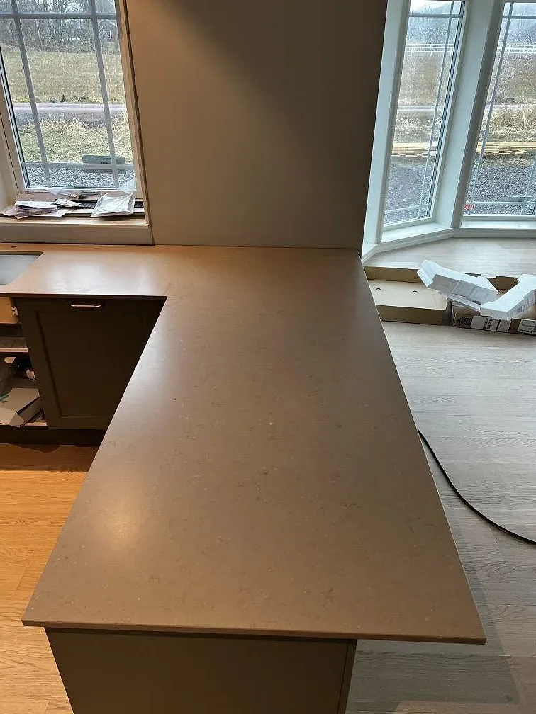 Köksbänkskiva och halvö i greige Silestone Coral Clay, matt Suede-yta, längs ett fönsterparti i ett kök under montering i Kärna.