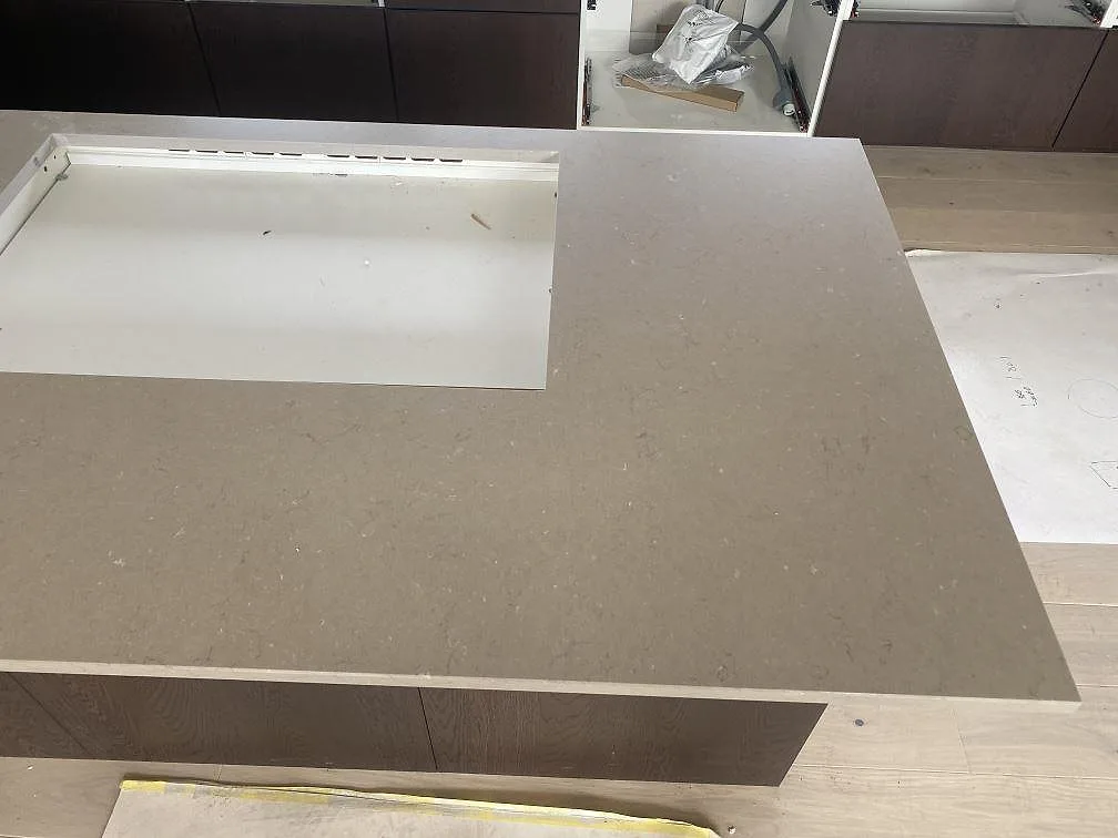 Ovanifrån av köksön i Silestone Coral Clay, matt greige komposit, med urtag för häll under pågående montering i ett kök i Kalmar.